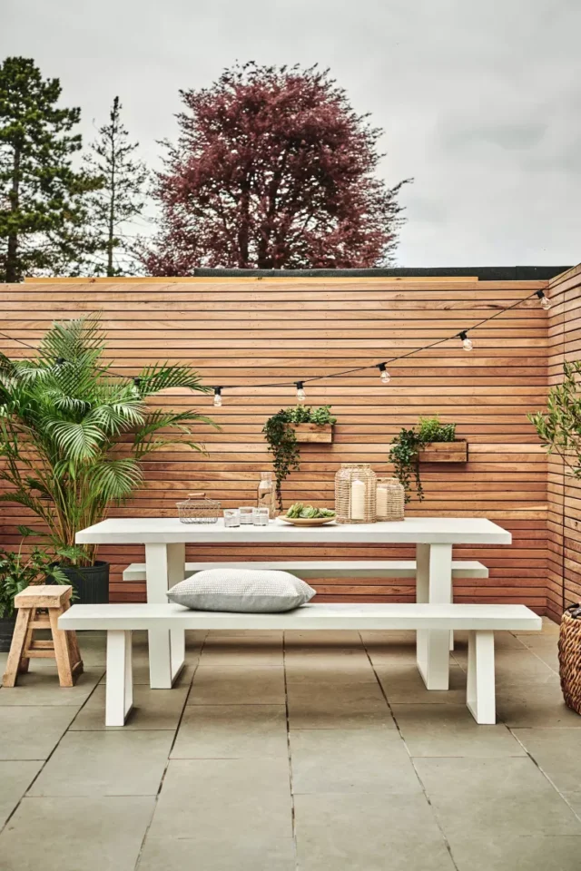 idee tavolo da giardino: panca bianca contro recinzione a pannelli