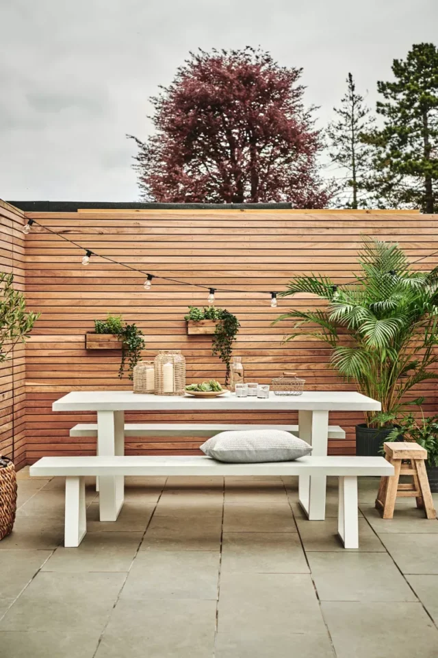 idee tavolo da giardino: panca bianca contro recinzione pannellata