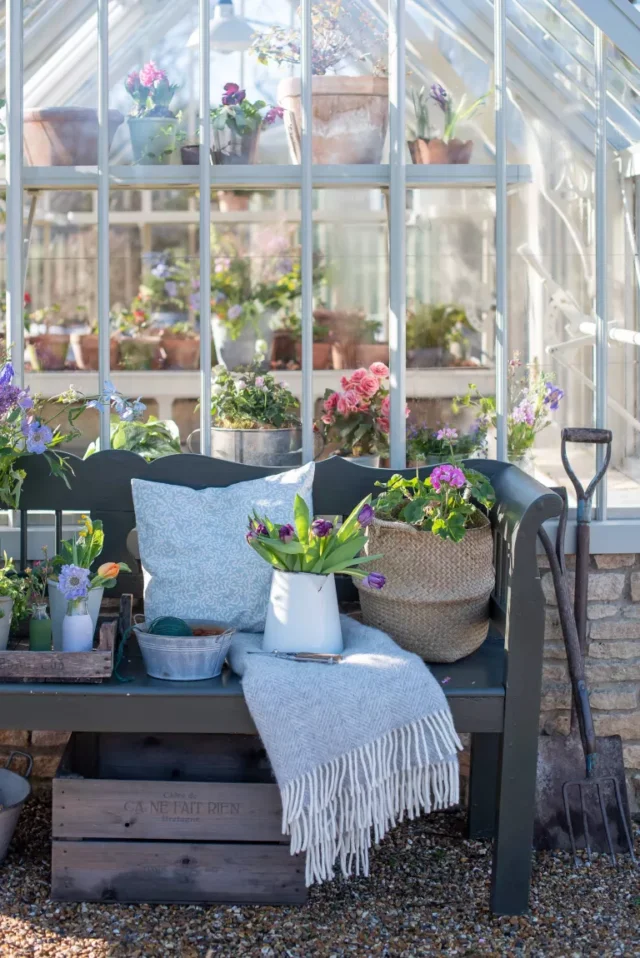 panchina da giardino dipinta all'interno di una serra con fiori colorati in vaso