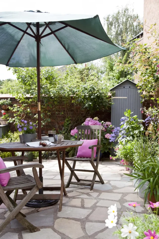 spazio patio con tavolo da pranzo, sedie e un ombrellone con cuscini rosa e fiori